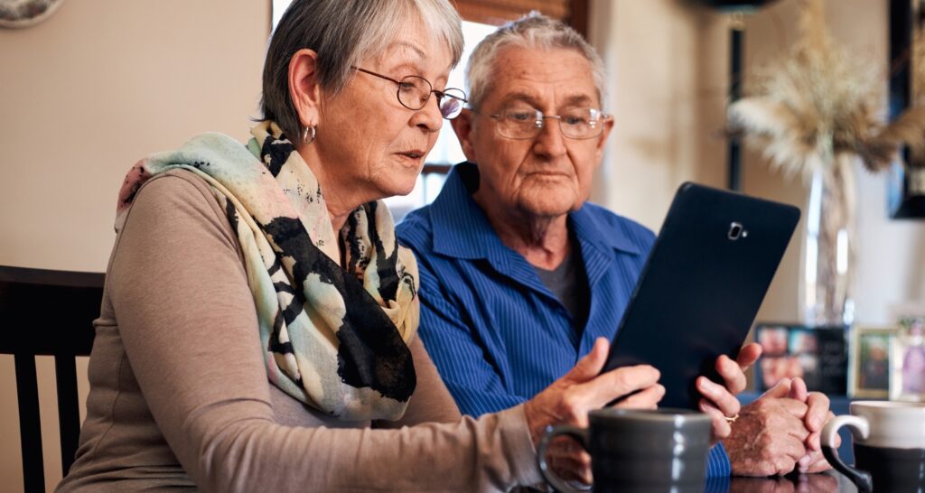 picture of older couple with glasses looking at an ipad together with coffee on the table
