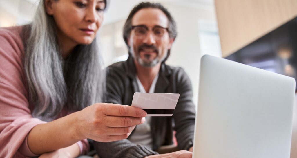 photo of woman holding a credit card with a man by a computer