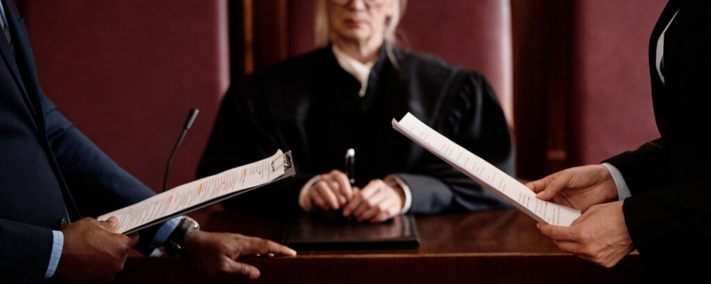 photo of an older female judge, with two people standing in front of her holding papers
