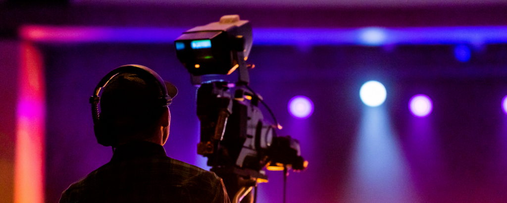 guy with a professional camera, looking towards a stage with headphones on.